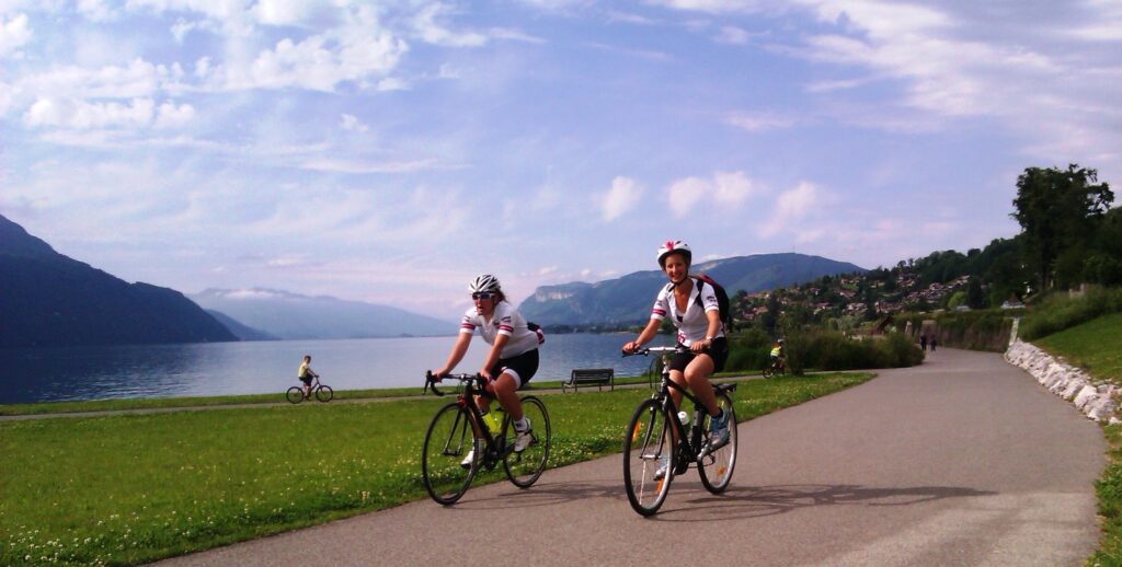 Two cyclists ride their bikes along a bikeway by Lac du Bourget during a cycle holiday